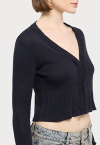 Czarny prążkowany krótki kardigan z głębokim dekoltem w kształcie V, długimi rękawami i teksturowanym wzorem dzianiny. Materiał wydaje się miękki i elastyczny.