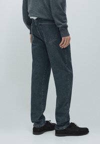 Ciemne dżinsy z denimu o luźnym kroju, z tylnymi kieszeniami i subtelnymi detalami przeszyć. Połączone z czarnymi zamszowymi butami.