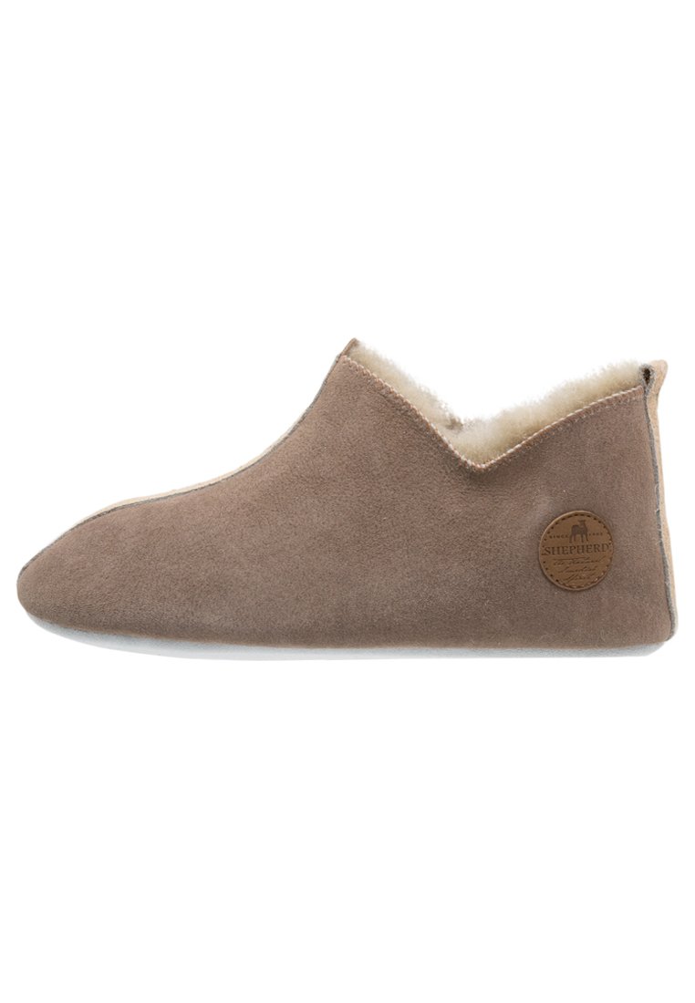 Brown suede slipper with soft fleece lining, low profile, rounded toe, and tonal stitching. Features a circular logo patch on the side.
