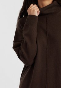 Pull à col roulé marron foncé en tricot doux et texturé. Caractéristiques : épaules tombantes et un détail de couture courant le long de l'avant.