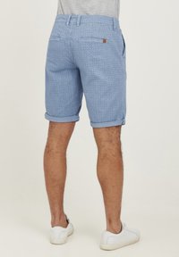 Shorts albastre deschis cu model, cu tivuri răsucite, fabricate dintr-un material moale, având două buzunare laterale și un buzunar la spate cu un mic etichetă logo.
