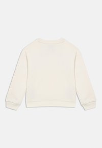 Κρεμ μπλούζα με μακριά μανίκια, ριμπ κουμπιά και στρίφωμα, κανονική λαιμόκοψη, εμφανίζεται από πίσω σε λευκό φόντο.