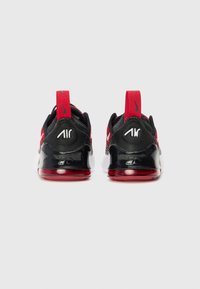 Sneakers Nike avec une tige noire, des accents rouges et une semelle blanche, présentant un coussin d'air visible et un détail de talon avec logo.