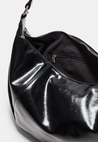 Czarna skórzana torebka o błyszczącym wykończeniu, z zamknięciem na zamek i wewnętrzną kieszenią. Projekt ma zaokrąglony kształt z jedną rączką.