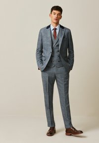 Three-piece suit with a blue and gray checkered pattern, tailored fit, navy shoulder accents, and brown leather shoes.