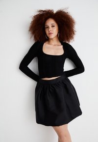 Top preto cropped de mangas longas com tecido texturizado e decote quadrado, combinado com uma saia mini plissada em cetim preto com cintura elástica.