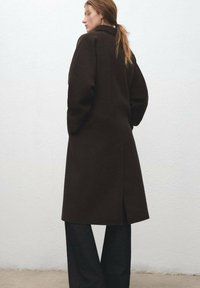 Bruine wollen jas met een getailleerde vorm, grote revers, zijslitten en een minimalistisch ontwerp, gecombineerd met een donkere broek.