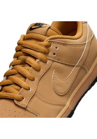 Gros plan sur une basket Nike couleur fauve avec des lacets assortis, le logo Nike Swoosh brodé, un col matelassé et un logo noir sur la languette.