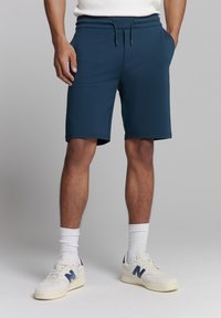 Marine blauwe sportbroekjes van soepele stof, met een elastische tailleband en een trekkoord. Voorzien van zijzakken en een normale pasvorm.