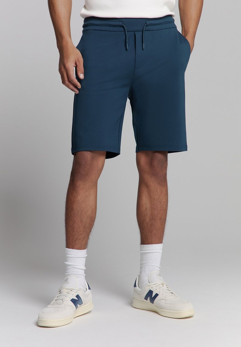 Marine blauwe sportbroekjes van soepele stof, met een elastische tailleband en een trekkoord. Voorzien van zijzakken en een normale pasvorm.