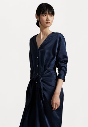 Vestido de satén azul marino con mangas largas, botones en la parte delantera y cintura anudada. Presenta un escote en V y una textura suave y brillante.