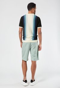 Polo shirt in zwart, marineblauw, lichtblauw en crèmekleurige strepen, gecombineerd met lichtgroene shorts. Model draagt witte sneakers.