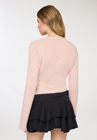 Maglione aderente a maniche lunghe di un rosa chiaro, con una texture morbida, abbinato a una gonna nera a balze stratificate, che mostra una vista posteriore chic.