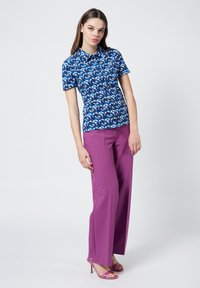 Short-sleeve blue patterned shirt with swirling designs, paired with high-waisted purple wide-leg trousers and matching pink heels.