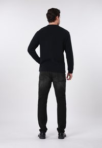 Μαύρο πουκάμισο με μακριά μανίκια σε συνδυασμό με σκούρο τζιν, με απλό σχέδιο και υφασμάτινη υφή, εμφανιζόμενο από την πίσω πλευρά χωρίς χαρακτηριστικές λεπτομέρειες.