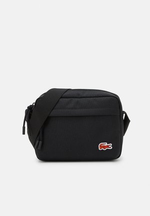 Sac bandoulière noir en tissu durable. Comprend une fermeture éclair, une sangle réglable et un logo crocodile orange brodé.