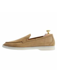 Mocassino beige in suede con punta leggermente appuntita e suola in gomma bianca. Presenta un laccio in oro e un design semplice senza motivi visibili.