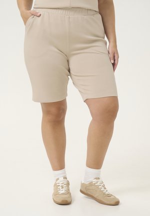 Beige elastic waist shorts with side pockets, soft fabric, and a smooth texture, paired with beige sneakers and white socks.