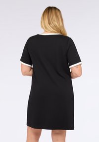 Vestido negro de manga corta con cuello redondo y ribete claro en contraste en las mangas. Tejido suave; corte a la altura de la rodilla.