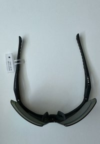 Gafas de sol deportivas negras con lentes tintados curvados y brazos texturizados, presentadas sobre un fondo gris claro liso.