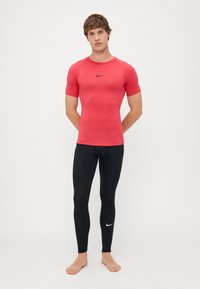 Rdeča športna majica s kratkimi rokavi z črnim logotipom Nike, v kombinaciji s črnimi leginami z belim Nike swooshom, zasnovana za zmogljivost in udobje.