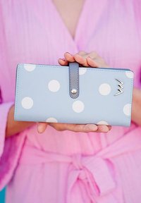 Light blue wallet with large white polka dots, gray strap, and metallic accent. Smooth texture with stitched edges. Dimensions not specified.