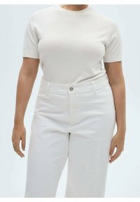 Vaaleanbeige lyhythihainen neulepaita yhdistettynä korkeavyötäröisiin valkoisiin farkk trousers, joissa on edessä nappikiinnitys ja rento malli.