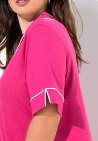 T-shirt rosa a maniche corte con rifiniture bianche sulle maniche. Presenta una vestibilità rilassata e una consistenza morbida, con un leggero accento agli spacchi delle maniche.