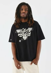 Zwarte oversized katoenen T-shirt met een grote witte grafische print met "PROJECT PARIS," verstrengelde harten en sterren. Korte mouwen en ronde hals.