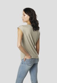 helehall hall lühikeste varrukatega topp, millel on lõdvestunud lõige, õrn ümar kaelus, pehme tekstuur ja väike tagatasku detail.