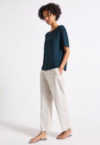 Top corto teal a maniche corte abbinato a pantaloni beige chiaro, morbidi e a vestibilità comoda, e sandali piatti con cinturini. L'outfit presenta tessuti morbidi e una silhouette rilassata.