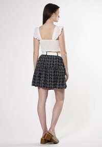 Top corto blanco con detalles de ojal y mangas con volantes, combinado con una falda negra de estampado floral. Unos zapatos de plataforma marrones completan el conjunto.