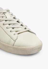 Sneaker beige chiaro con una tomaia in suede liscio, lacci piatti e una suola in gomma cremoso testurizzata. Punta arrotondata e design minimalista.