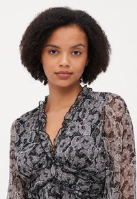 Svart og grå, gjennomsiktig bluse med paisleymønster, volangkrage og lange ermer, som fremhever en delikat tekstur og design.