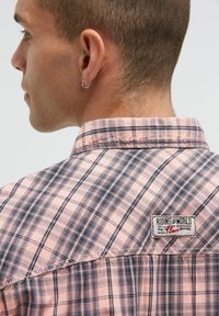 Karierte kurzärmlige Bluse in Pink und Marineblau, mit Kragen und Markenetikett auf der Rückseite, sichtbaren Nähten und Karotextur.