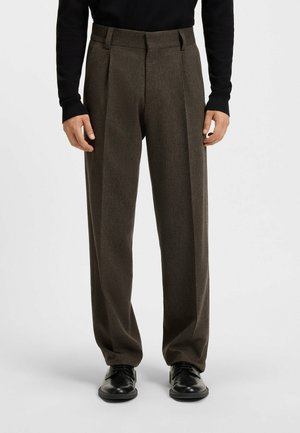Brown, pleated dress pants made of textured fabric, featuring a high waist and straight leg design, paired with black shoes.