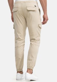Beige Cargo-Hosen mit elastischem Bund, zulaufenden Beinen und Cargo-Taschen. Das Material ist leichter Stoff mit glatter Textur.