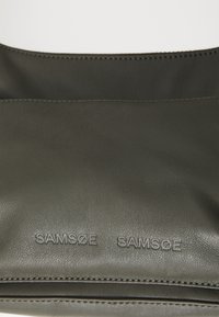 Dark green leather bag with a smooth texture. Featuring embossed "SAMSOE SAMSOE" logo and contrasting stitching detail along the edges.