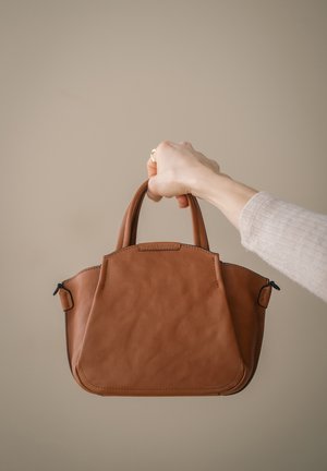 Braune Lederhandtasche mit zwei kurzen Griffen, einer strukturierten Form und sichtbaren Nähten. Reißverschlussdetail auf einer Seite und eine strukturierte Oberfläche.