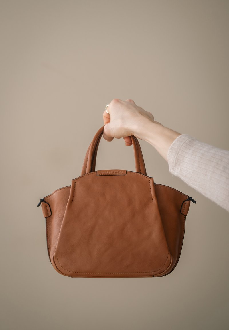 Braune Lederhandtasche mit zwei kurzen Griffen, einer strukturierten Form und sichtbaren Nähten. Reißverschlussdetail auf einer Seite und eine strukturierte Oberfläche.