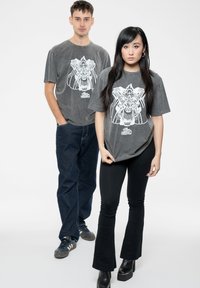 Gray t-shirts with a white graphic design featuring a lion's head. One person wears dark jeans; the other wears black flared pants and platform boots.