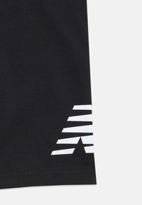 Zwarte stof met een gedeeltelijk zichtbaar wit geometrisch patroon dat bestaat uit gestapelde trapeziums nabij de rand.