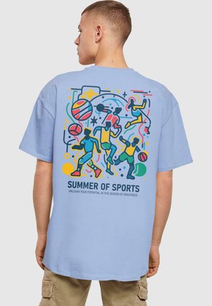 Lyseblå t-shirt med et farverigt grafisk design af atleter, basketballer og teksten "SOMMEREN AF SPORT" i sort, med legende designelementer.