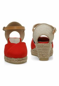 Wedge espadrilles in tela rossa con suola in juta, cinturino alla caviglia color cammello e design aperto sul retro. Tessuto intrecciato texturizzato sul tacco.