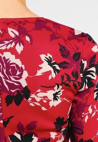 Tissu rouge présentant un motif floral aux nuances de rose, blanc et noir. Le design comprend de grandes roses et des accents feuillus sombres.