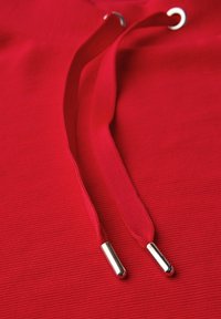 Tessuto rosso con una texture a coste, con due cordini rossi con punte metalliche, posizionati su uno sfondo liscio e vivace.