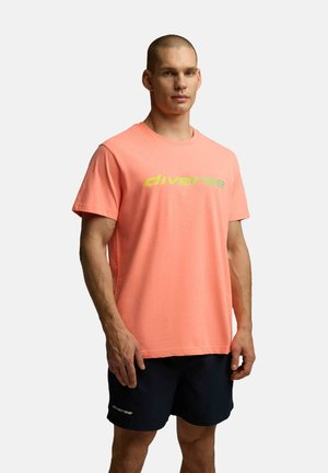 T-shirt z krótkim rękawem, okrągłym dekoltem w jasnym koralowym kolorze z napisem "różnorodny" w żółto-zielonym kolorze. Wykonany z miękkiego materiału, o luźnym kroju i gładkiej teksturze.