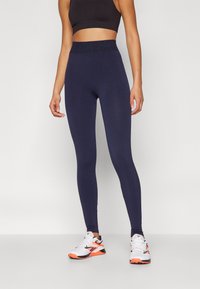 Leggings navy con una vita alta ed elastica e una texture liscia, abbinati a sneakers bianche e arancioni con accenti neri.