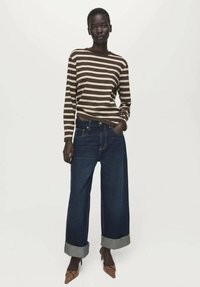 Prugasta smeđa i kremasta majica dugih rukava uparena s tamnoplavim širokim trapericama s preklopljenim rubovima i smeđim cipelama sa špicom.