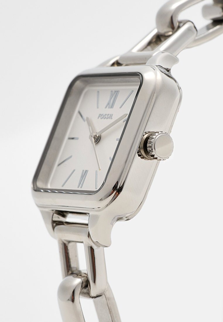 Orologio da polso in metallo argentato con quadrante quadrato, dial bianco, numeri romani e un bracciale a catena texturizzata. Presenta una corona per le regolazioni.